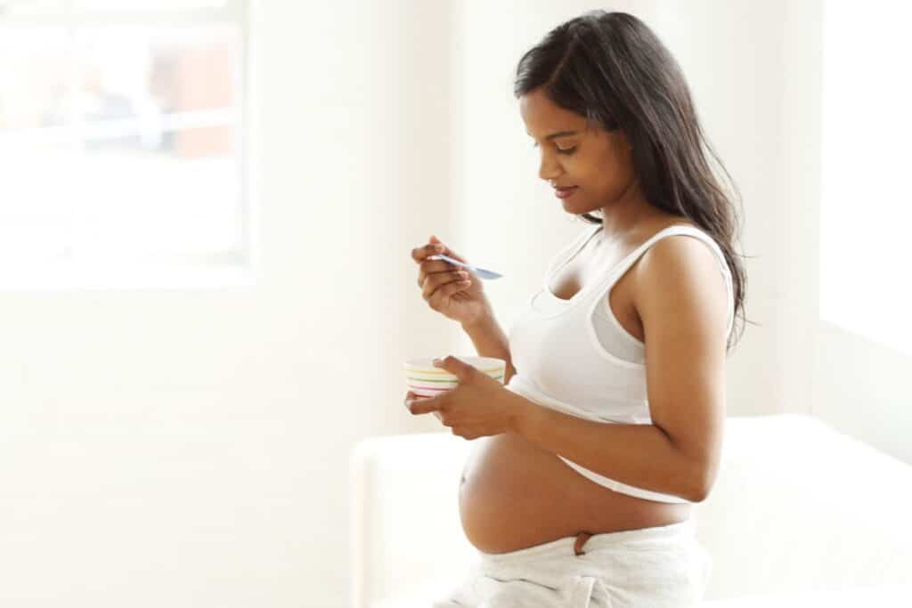 Young pregnant woman snacking on yogurt and granola 